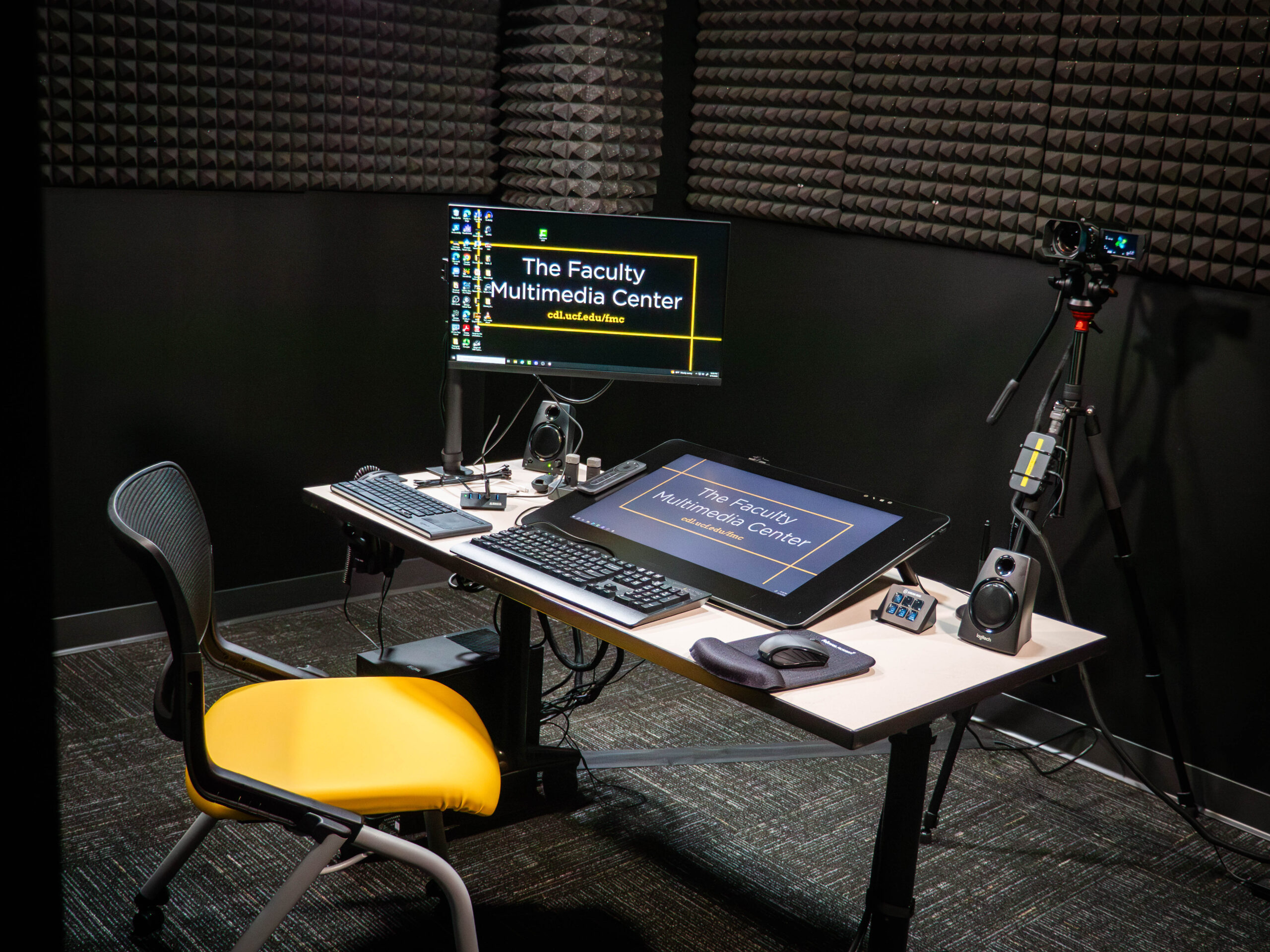A soundproof room with a camera, two monitors and a black and yellow chair. 